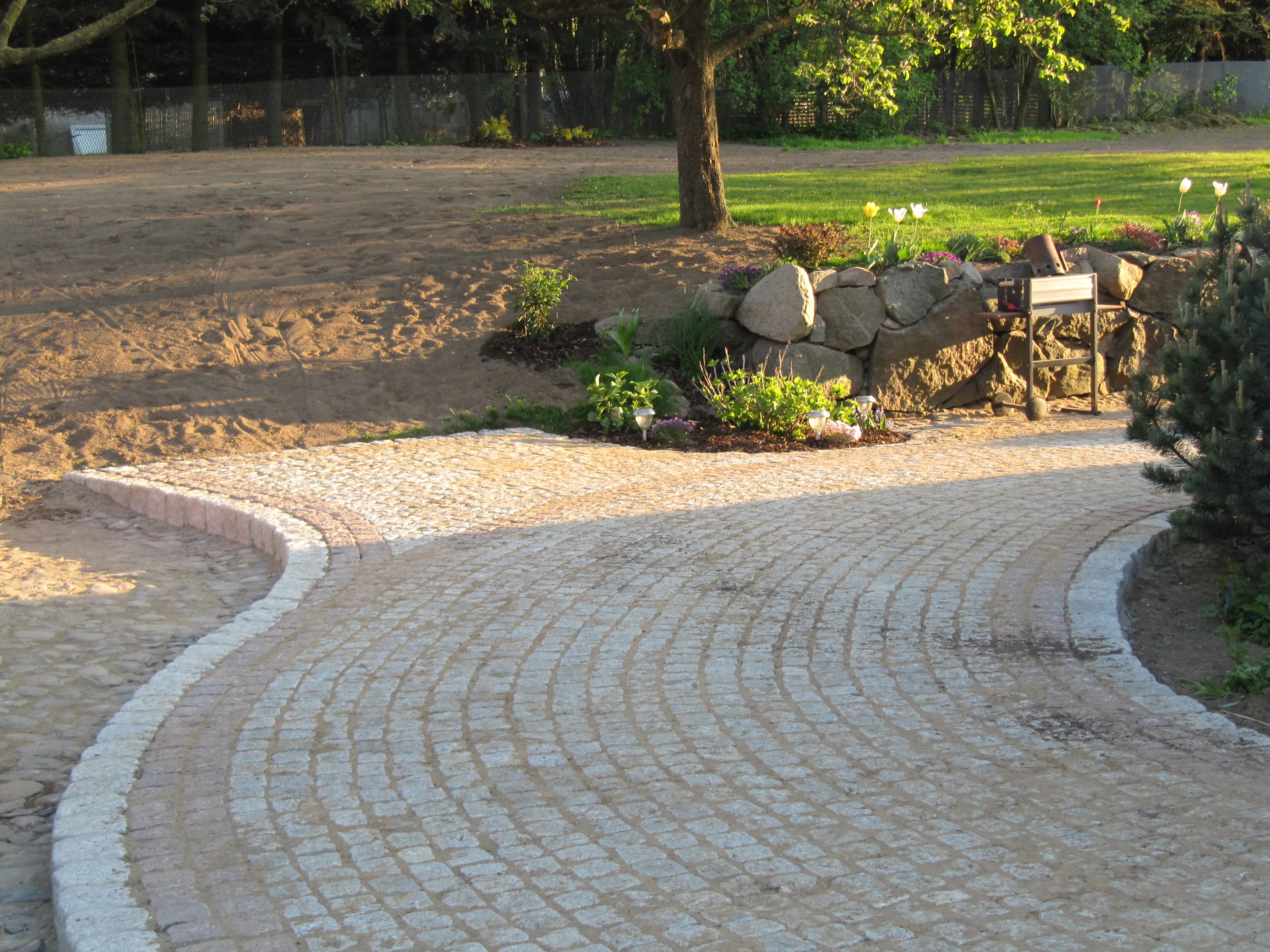 Geschwungener Weg aus Granit-Kleinpflaster mit Natursteinmauer und Beet in einem Garten in Schönberg