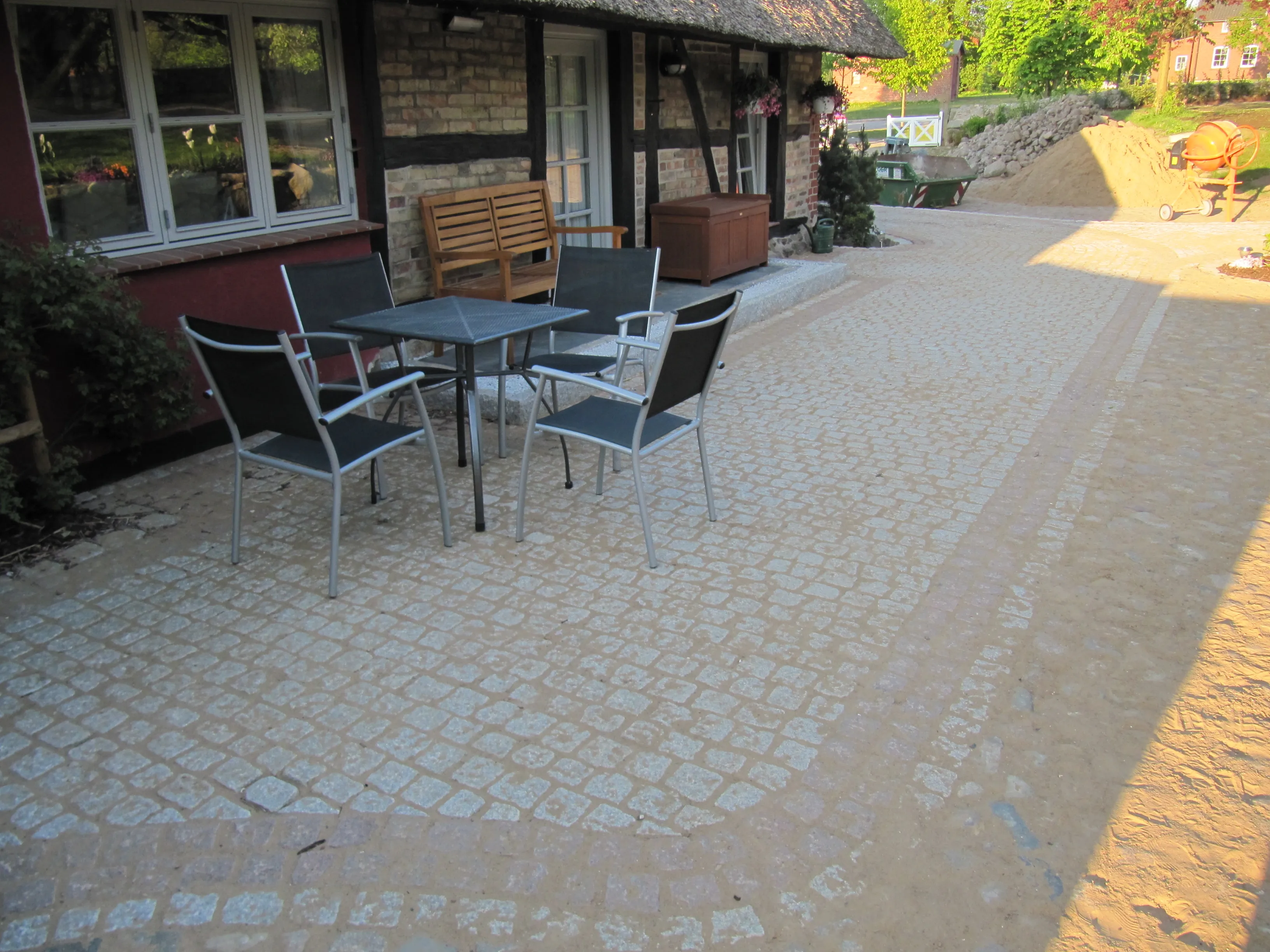 Sitzterrasse aus hellem Kleinpflaster mit Tisch und Stühlen vor einem Reetdachhaus
